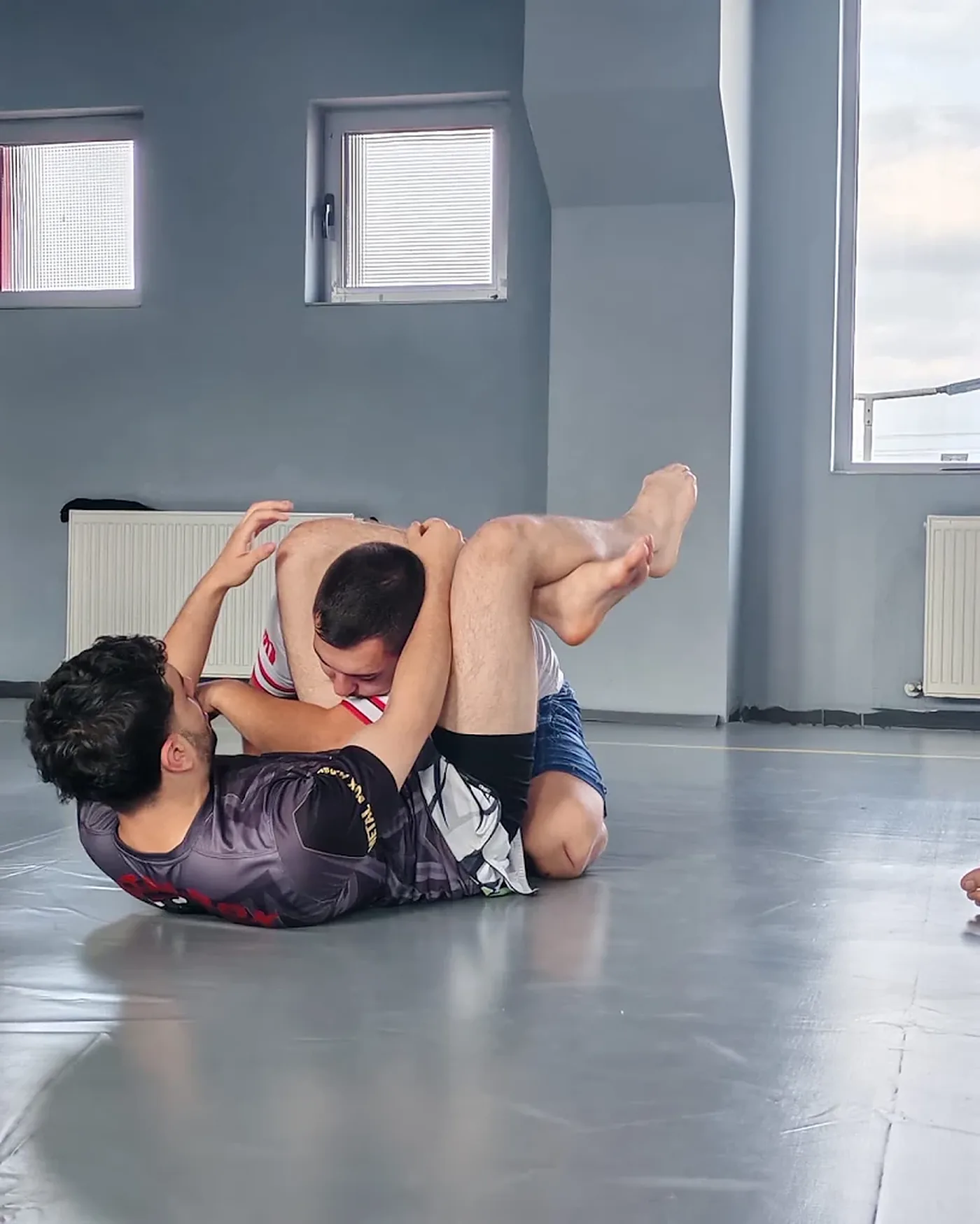 Doi practicanți de grappling lucrând o poziție la sol pe salteaua clubului